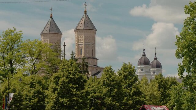 The Monastery of the Holy Three Hierarchs stands tall among trees in Iasi. Sunlight shines on the buildings, creating a beautiful urban view that captures attention.