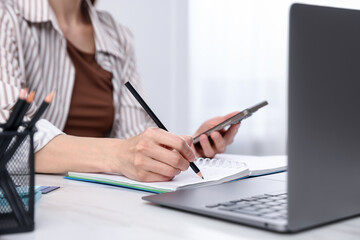 Fototapeta premium Young woman using laptop and smartphone at workplace in kitchen, closeup