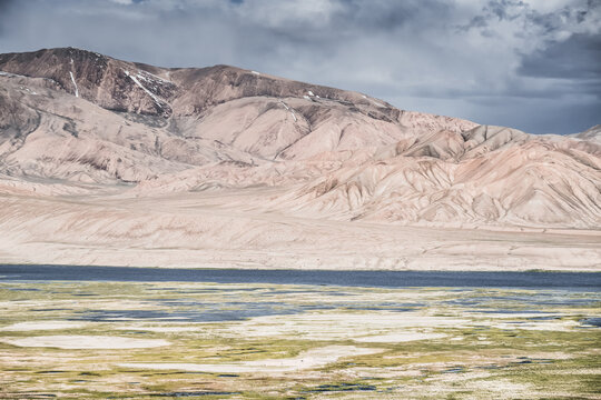 Landscape in the Pamir Mountains in valley with green grassy meadows and pastures, mountain range rises in the Tien Shan Mountains, panoramic landscape for background