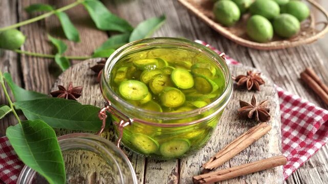 Hands adding sliced unripe green walnuts into a jar with alcohol - preparation of homemade nut liqueur or tincture