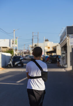 Rear view of an 11-year-old boy with a broken arm in a black medical sling walking down a street during a summer vacation in Kato Gouves, Crete, Greece