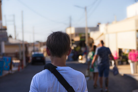 Rear view of an 11-year-old boy with a broken arm in a black medical sling walking down a street during a summer vacation in Kato Gouves, Crete, Greece