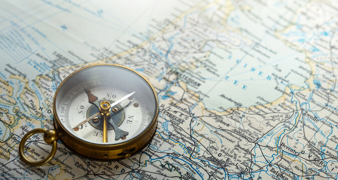 Vintage brass compass on an old geographic map close up. Antique navigation instrument for travel, exploration, geography and discovery concept. 