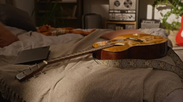 Acoustic guitar with patterned strap and closed laptop lying on bed in home music production studio.Online music education, songwriting courses, and creative freelance lifestyle marketing