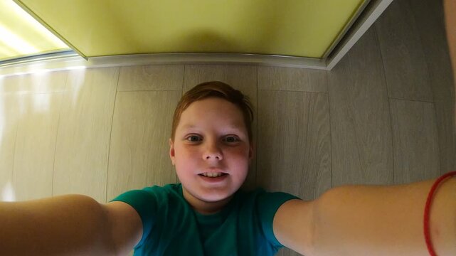 Male face of little smiling red-haired boy with freckles lying on the floor in room and filming himself on GoPro. Portrait of happy ginger kid having fun at home and taking selfie photo on smartphone