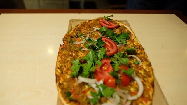 Fresh lahmacun served on a wooden board with tomato, onion and parsley. Close-up of traditional Turkish cuisine in a restaurant, showing local food cultures, appetizing presentation and lunch concept.