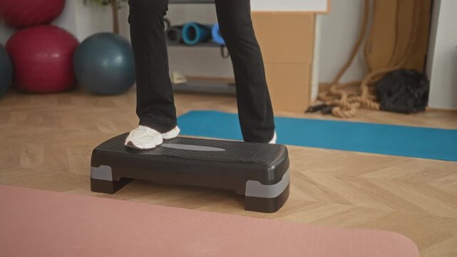 Woman stepping right foot onto a fitness stepper platform while wearing sneakers and leggings in a studio; fitness focus.