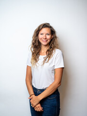 Fototapeta premium Studio portrait of a mid-thirties woman on a white backdrop wearing a white t-shirt and dark blue jeans, with dark blonde wavy hair and a happy, smiling expression.