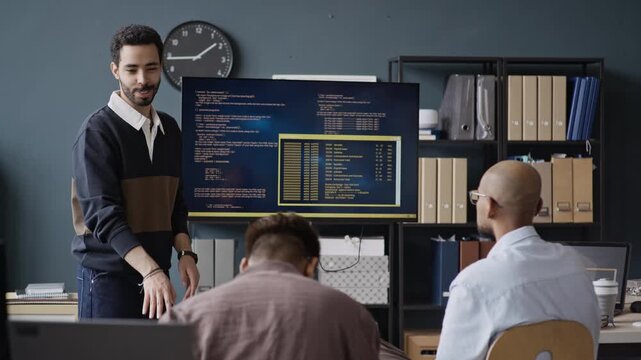 Medium shot of young Middle Eastern man presenting programming code on screen to multiethnic colleagues in IT office. Clip is suitable for tech startup marketing or coding education ads