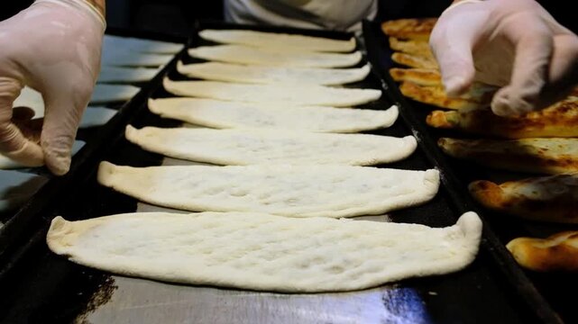 Prepared pides lined up on black baking trays in a bakery kitchen, ready for the oven. Food production, tray arrangement, baking preparation and professional kitchen workflow concept.