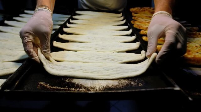 Prepared pides lined up on black baking trays in a bakery kitchen, ready for the oven. Food production, tray arrangement, baking preparation and professional kitchen workflow concept.