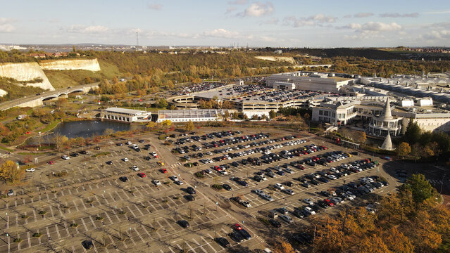 Aerial view of the Bluewater shopping centre surrounded by extensive parking lots, lush greenery, and chalk cliffs in Dartford, England, United Kingdom.