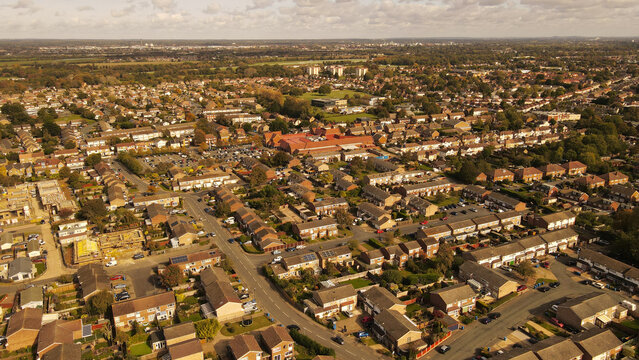 Aerial view of a suburban residential neighborhood featuring rows of houses, winding streets, and green spaces under a cloudy sky in England, United Kingdom.