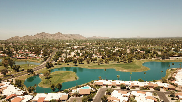 Aerial view of a residential neighborhood with a winding lake and golf course surrounded by palm trees and desert mountains, Phoenix, Arizona, United States.
