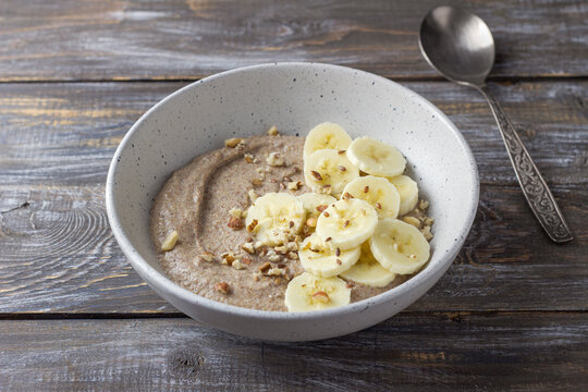 Healthy flaxseed porridge topped with banana slices, chopped nuts and seeds in a ceramic bowl. Nutritious breakfast with natural ingredients, copy space