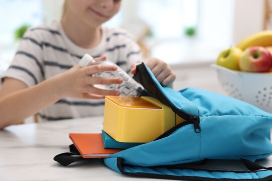 Girl putting bottle of water into backpack in kitchen, closeup. Healthy school lunch