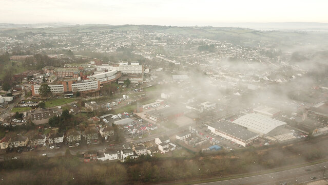 Aerial view of a large hospital complex and surrounding industrial buildings partially obscured by morning fog in Torquay, England, United Kingdom.