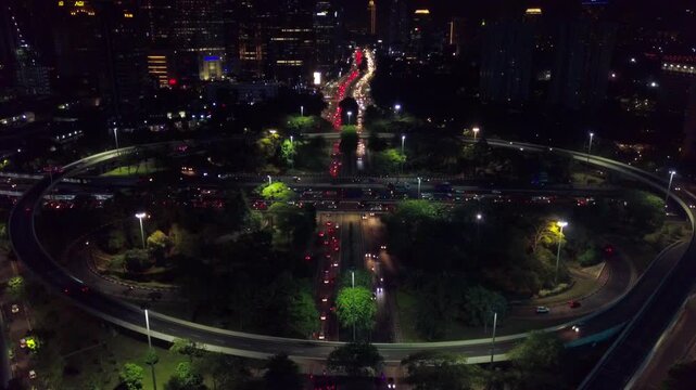 Aerial night view of the Semanggi Interchange in Jakarta, Indonesia, showing red and white light trails from vehicles moving through the cloverleaf junction