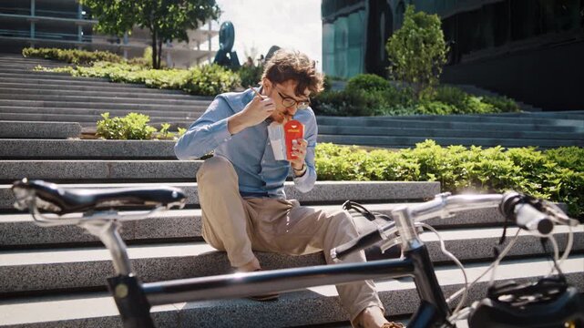 Man eats takeaway lunch on stone steps by bicycle against office