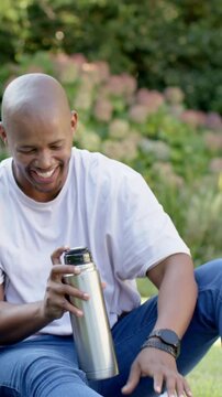Vertical video: Reaching for thermos, man opening cap on lawn, sipping cap, laughing toward friend