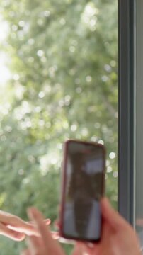 Vertical video: Raising finger woman in long-sleeve top tapping phone near window, red case