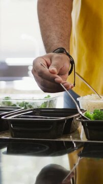 Vertical video: Yellow-sleeved hand filling bins of broccoli, rice at counter, copy space
