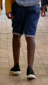 Vertical video: Walking pupil in yellow top, blue backpack to school entry, peer touching shoulder