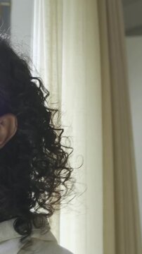 Vertical video: Hand reaching tucking hair subject in hoodie by window turning, smiling, copy space