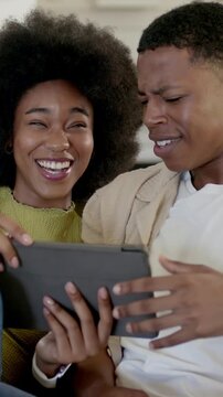 Vertical video: Smiling woman viewing tablet content, couple in casual clothes laughing on couch