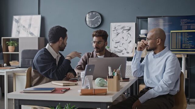 Medium long shot of motivated young diverse male developers discussing programming code on laptop screen in office. Perfect for IT recruitment campaigns and software engineering presentations