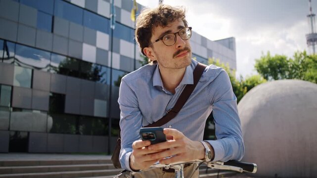 Man checks smartphone while leaning over bicycle near office