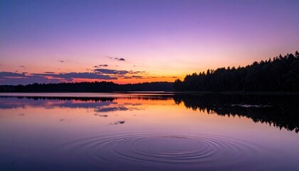 Naklejka premium Serene sunset over a calm lake with vibrant purple and orange hues reflected on the water surface