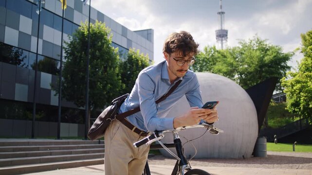 Man waits holding smartphone near bicycle and white sculpture