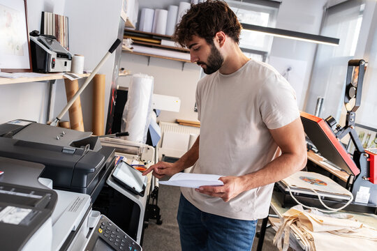 A print shop worker prepares a job on a digital color printer, checking settings and print files before production. The scene highlights attention to detail and the daily workflow of professional prin