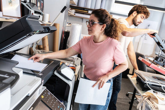 A print shop worker prepares a job on a digital color printer, checking settings and print files before production. The scene highlights attention to detail and the daily workflow of professional prin