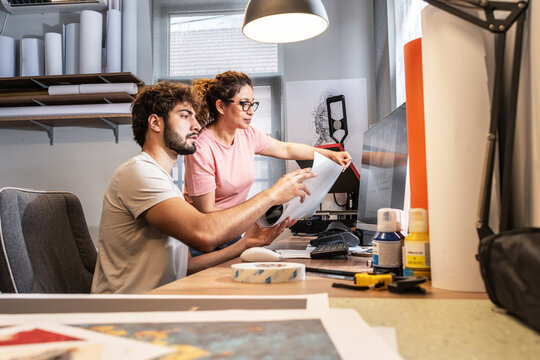 Two colleagues in a print shop work together on preparing a branding project for production. They review designs and print materials, making sure everything is ready before printing.