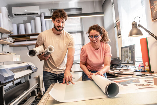 Two colleagues in a print shop work together on preparing a branding project for production. They review designs and print materials, making sure everything is ready before printing.
