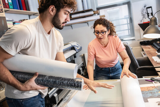 Two colleagues in a print shop work together on preparing a branding project for production. They review designs and print materials, making sure everything is ready before printing.