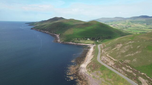 Drone aerial scenic route l footage of a car driving along a winding coastal road in dingle penisnula ireland, with lush green hills meeting the deep blue atlantic ocean
