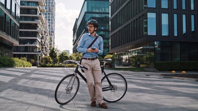 Man checks smartphone leaning on bicycle in modern office plaza