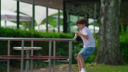 Naklejka premium Young boy climbing onto playground carousel while preparing to spin ride, playful childhood moment expressing anticipation curiosity and outdoor activity