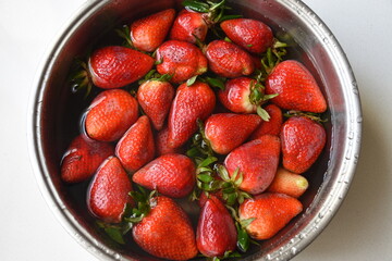 Fresh ripe strawberries soaking in water inside a metal bowl, showcasing healthy food preparation, fruit washing, cleanliness, freshness, and organic nutrition in a simple kitchen setting. © Nret