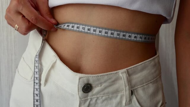 Woman measuring waist with tape showing body transformation and weight loss progress concept