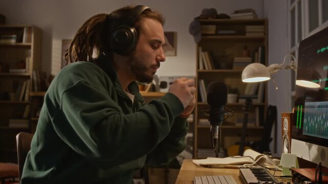 Caucasian young man putting on headphones and playing harmonica into microphone in home studio while recording new song. Promoting online music education, podcasting, or remote creative work