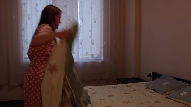 Young woman making a bed in a dimly lit bedroom