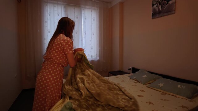 Young woman making a bed in a dimly lit bedroom