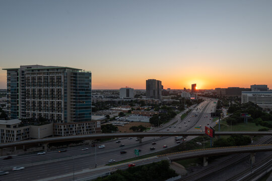 Orange and yellow glow on the horizon as the sun sets behind a building on Interstate 35 north of downtown Dallas, Texas.