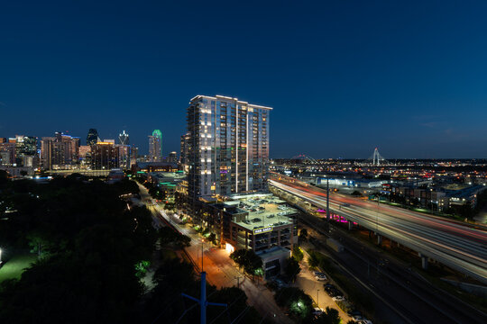 Light trails from cars passing by the lit up skyline of Dallas, Texas on I-35 just after sunset on a clear summer night.
