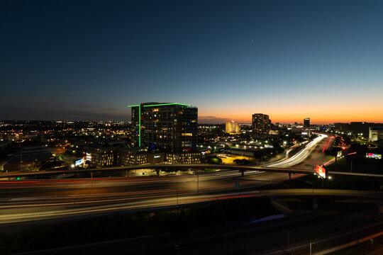 Light trails of vehicles driving through Dallas, Texas on Interstate 35 in Dallas, Texas as the sun sets on the distant horizon.