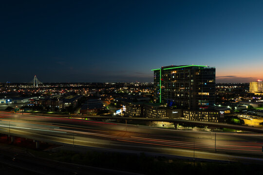 Light trails of vehicles driving through Dallas, Texas on Interstate 35 in Dallas, Texas as the sun sets on the distant horizon.